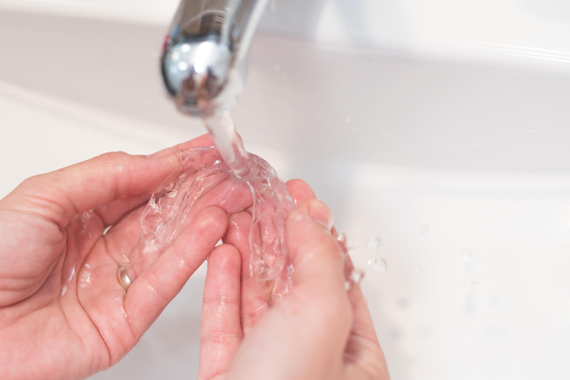 Zwei Hände einer Person, die ihre Zahnschiene unter fließendem Wasser wäscht.